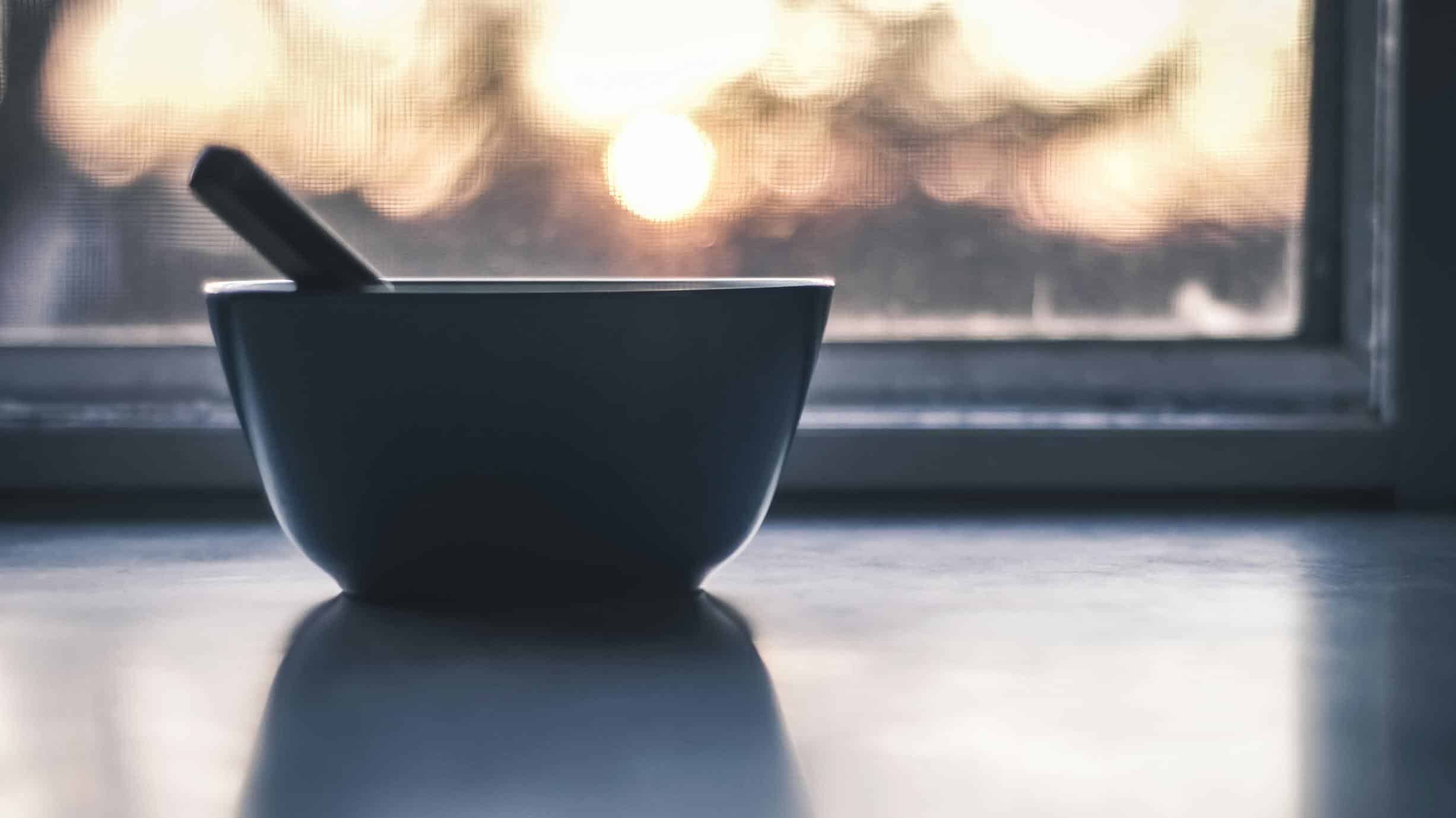 A minimalist still life photo of a bowl with a spoon by a window during sunrise.