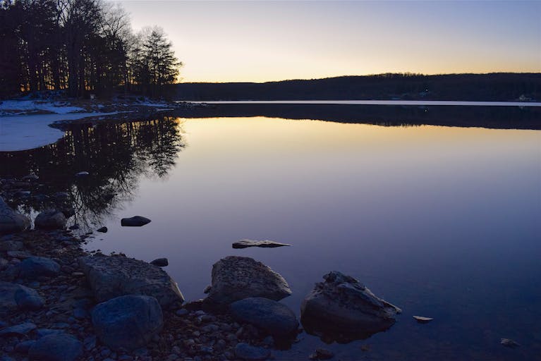 Tranquil twilight scene with calm lake and rocky shore reflecting the fading light.