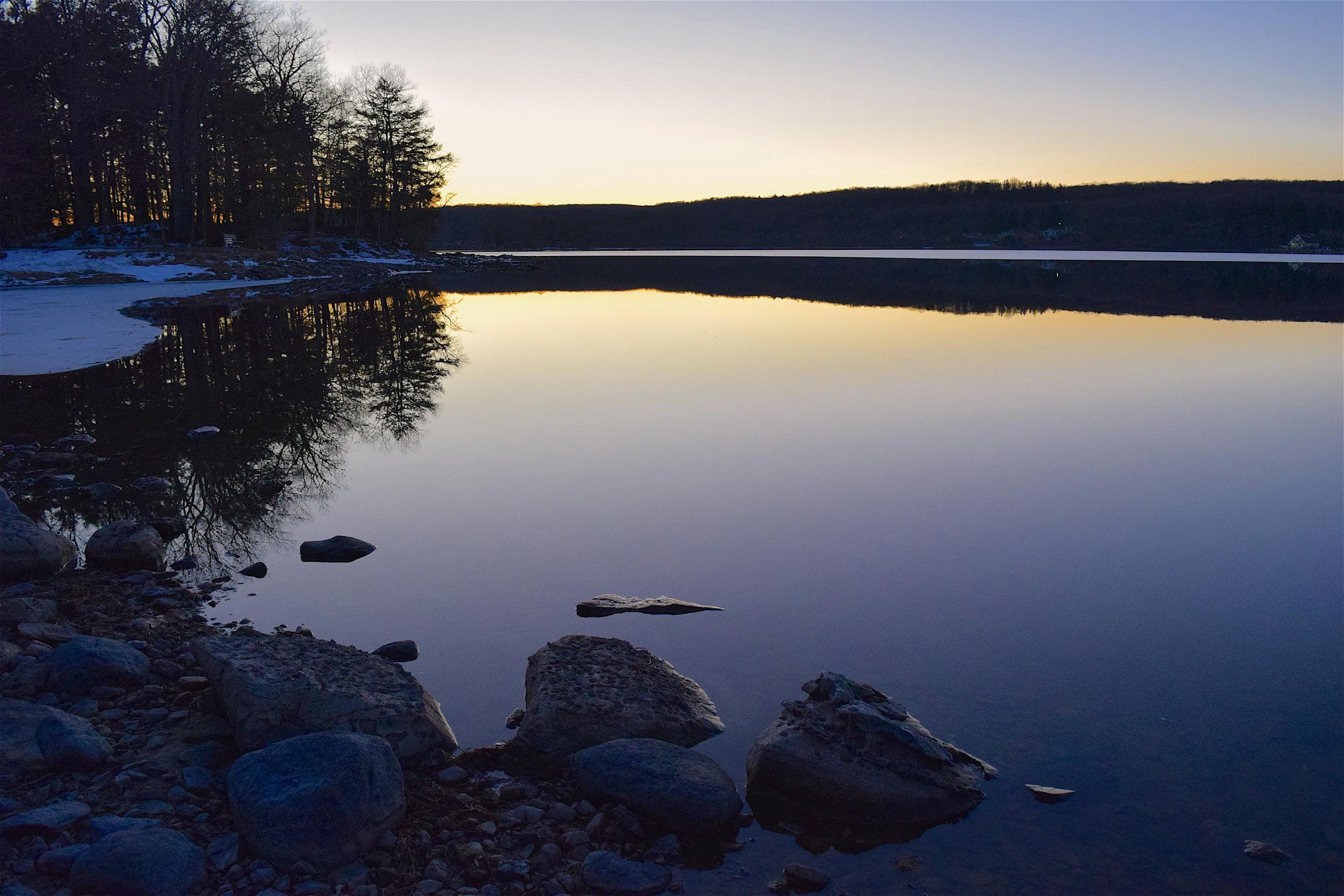 Tranquil twilight scene with calm lake and rocky shore reflecting the fading light.