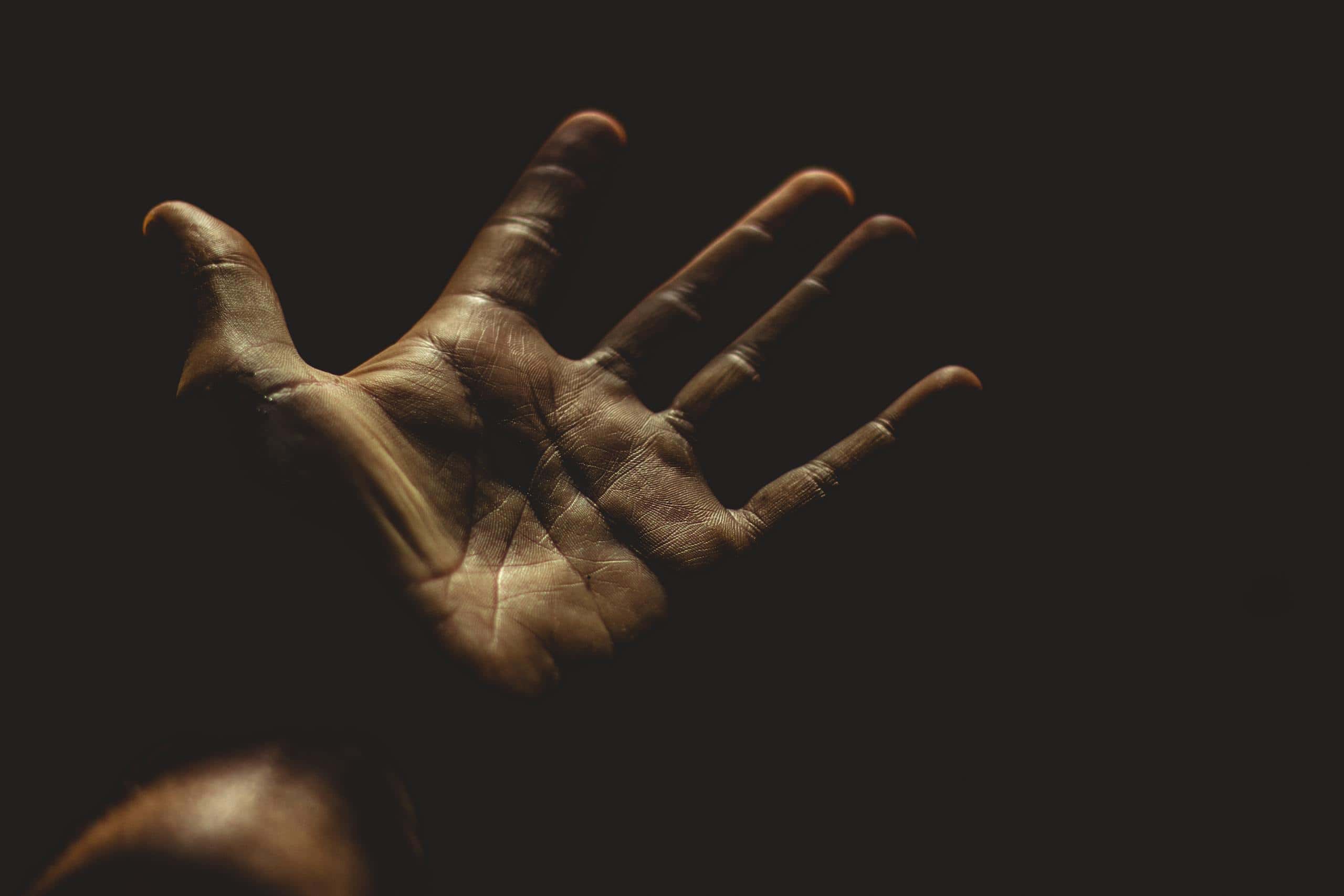 A powerful silhouette of an outstretched palm against a dark background, evoking emotion.